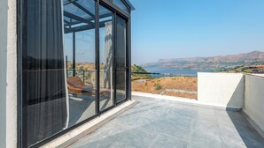 A balcony with a glass door, a view of a lake, and a hilly landscape. - ELIVAAS White House 4BHK Villa With Pool (Igatpuri)