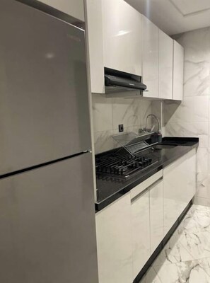 Eine Küche mit modernem Design, ausgestattet mit einem Edelstahl-Kühlschrank, einer schwarzen Kochplatte und weißen Schränken.