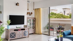 A modern living room with a flat-screen TV, wooden cabinet, and a glass coffee table. - Vita by Dia hotels And Homes  (Nerul)