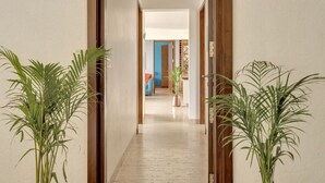 A hallway with a light-colored floor, wooden doors, and potted plants on either side. - Vita by Dia hotels And Homes  (Nerul)