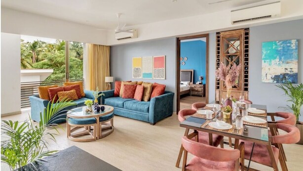 A spacious living area with a blue sofa, a round coffee table, and a dining table set for four. - Vita by Dia hotels And Homes  (Nerul)