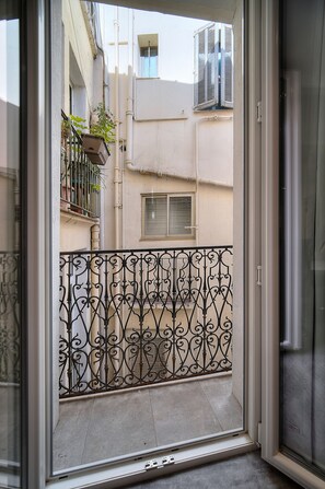 Blick vom Balkon mit schmiedeeisernem Geländer, einem Blumentopf und einem Gebäude mit Fenster und Klimaanlage im Hintergrund.