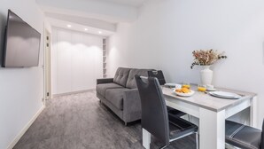 A modern, minimalist living space with a grey sofa, a dining table with chairs, and a flat-screen TV mounted on the wall. - 2 PIECES MODERN FELIX FAURE A1B232 (Cannes)
