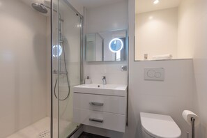 A modern bathroom with a glass shower enclosure, a white sink with a mirror above it, and a toilet with a paper towel holder. - 2-ROOM MODERN APARTMENT, FELIX FAURE, A1B232 (Cannes)