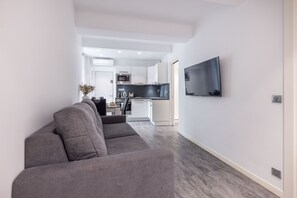 A modern living room with a grey sofa, a flat-screen TV mounted on the wall, and a kitchen in the background. - 2-ROOM MODERN APARTMENT, FELIX FAURE, A1B232 (Cannes)