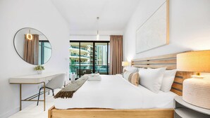 Habitación de hotel moderna con una cama grande, un escritorio, una silla, un espejo redondo, una lámpara de noche y vistas de edificios altos.