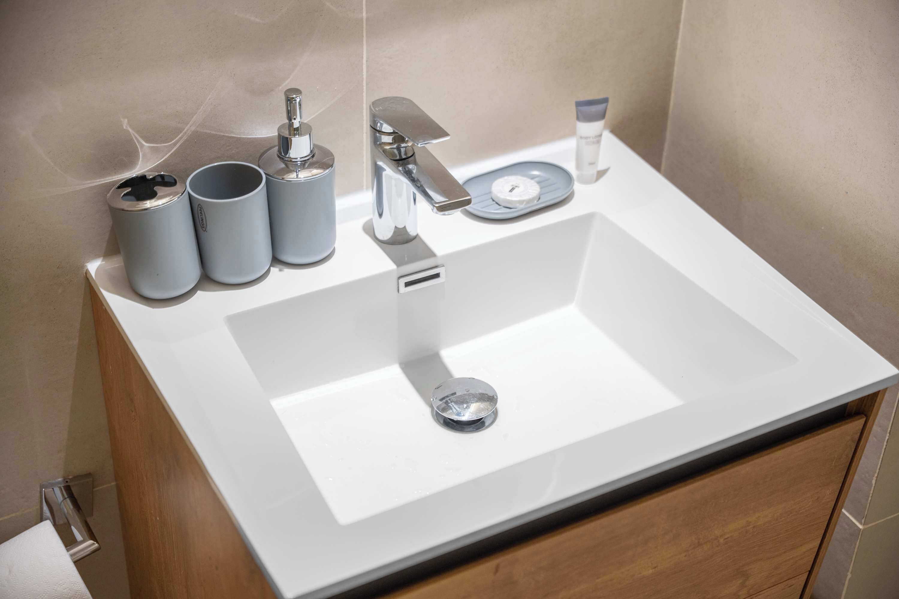 Un baño moderno con un lavamanos blanco, grifo cromado y dos recipientes cilíndricos.
