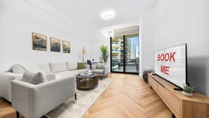 Una sala de estar moderna con un sofá, una mesa de centro y un televisor que muestra 'BOOK ME'.