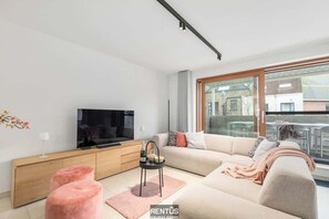 A modern living room with a sofa, TV, and a small table with a bottle and candles. - Villa 85 - stylish stay for 6 in a car-free domain in Ostend (Oostende)