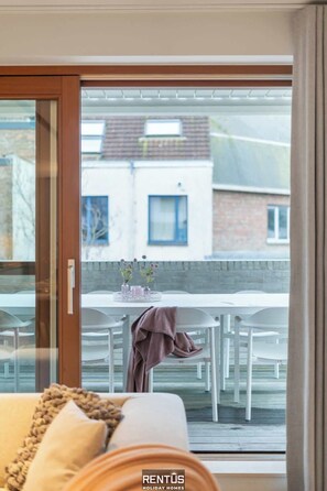 A modern living room with a sliding glass door leading to a balcony. The balcony has a white table with chairs and a vase of flowers. - Villa 85 - stylish stay for 6 in a car-free domain in Ostend (Oostende)
