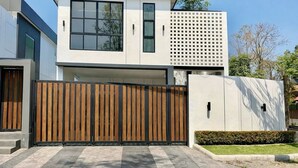A modern two-story house with a flat roof, large windows, and a wooden fence. - วิลลาพร้อมสระว่ายน้ำ 4 ห้องนอน 4 ห้องน้ำ พร้อมสิ่งอำนวยความสะดวก (Tambon San Phak Wan)