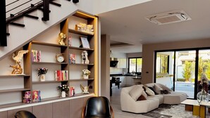 A modern living room with a sectional sofa, two leather chairs, a coffee table, and a built-in bookshelf with decorative items. - วิลลาพร้อมสระว่ายน้ำ 4 ห้องนอน 4 ห้องน้ำ พร้อมสิ่งอำนวยความสะดวก (Tambon San Phak Wan)