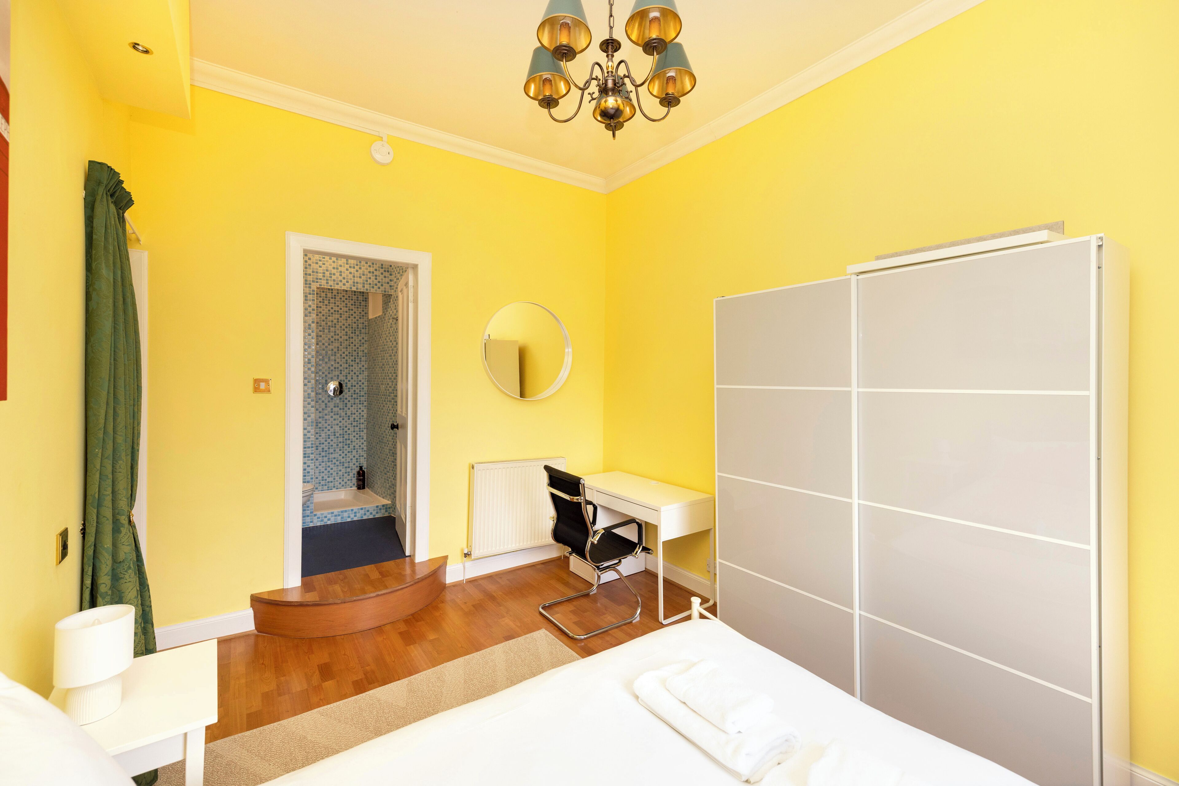 Ein Hotelzimmer mit Bett, Schreibtisch, Stuhl, Spiegel, Heizkörper und Duschbereich.