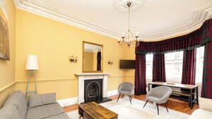A living room with a sofa, coffee table, fireplace, and a television. - Stylish Southside Flat Near Old Town (Edinburgh)