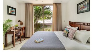 A hotel room with a bed, a desk, a chair, a ceiling fan, and a view of palm trees through the window. - Viora by Dia hotels And Homes  (Nerul)