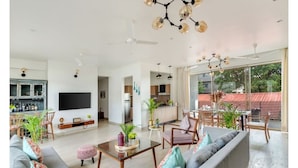 A modern living room with a sofa, coffee table, and chairs. There is a kitchen area with a dining table and chairs. A flat-screen TV is mounted on the wall. - Viora by Dia hotels And Homes  (Nerul)