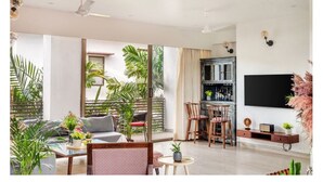 A spacious living area with a balcony, a dining set, and a TV mounted on the wall. - Viora by Dia hotels And Homes  (Nerul)