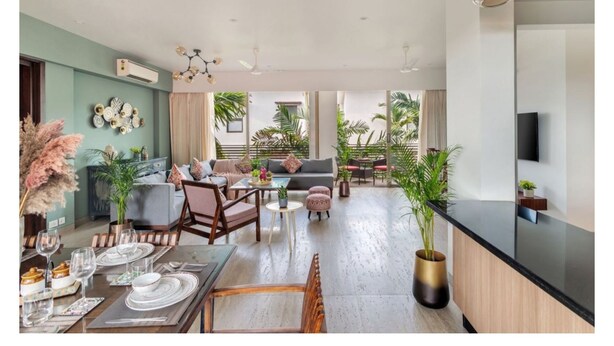 A spacious living area with a dining set, sofas, and a kitchen area with a black countertop. - Viora by Dia hotels And Homes  (Nerul)