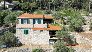 A stone house with a tiled roof, green shutters, and a stone staircase leading to a porch.