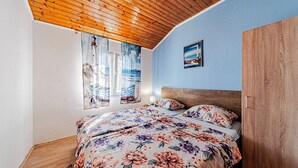 Une chambre avec un plafond en bois, un lit recouvert d’une literie à motifs floraux, une fenêtre avec des rideaux et un tableau accroché au mur.
