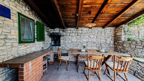 A rustic outdoor dining area with a stone wall, wooden ceiling, and a brick counter. - Robinson’s House Maya by Villas Guide (Blato)