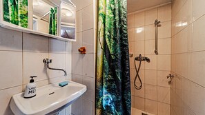 A bathroom with a sink, mirror, shower, and a forest-themed shower curtain. - Robinson’s House Maya by Villas Guide (Blato)