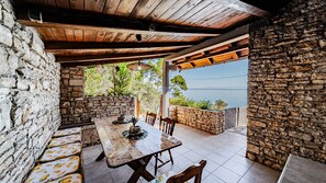 A stone-walled patio with a wooden table and chairs, overlooking a body of water.