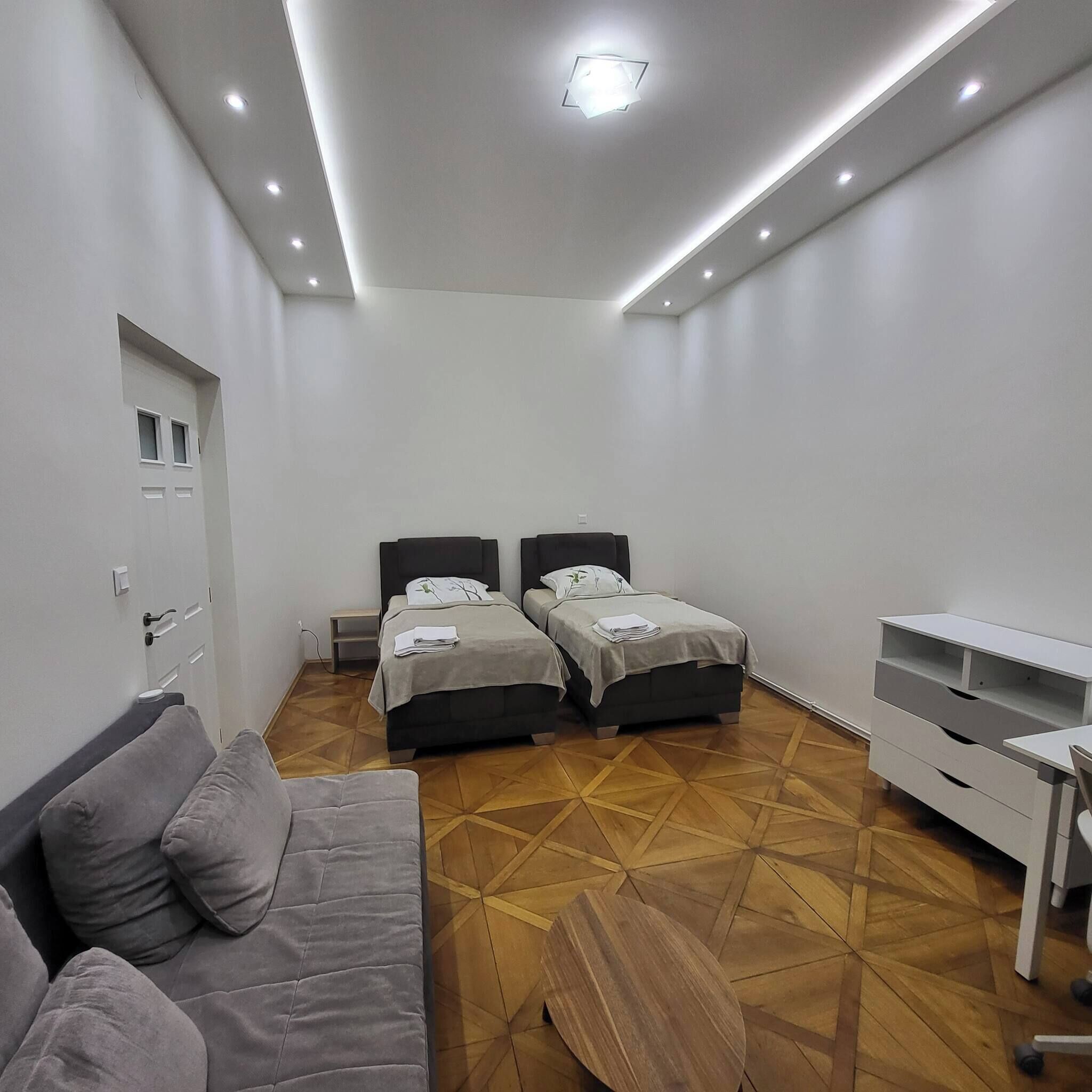 A modern bedroom with two beds, a sofa, a TV stand, and a patterned floor.