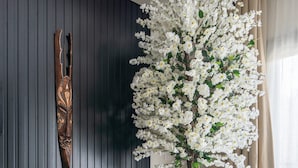 Een moderne woonkamer met een donkere houten wand, een houten bankje, een potplant en een grote kunstboom met witte bloemen.
