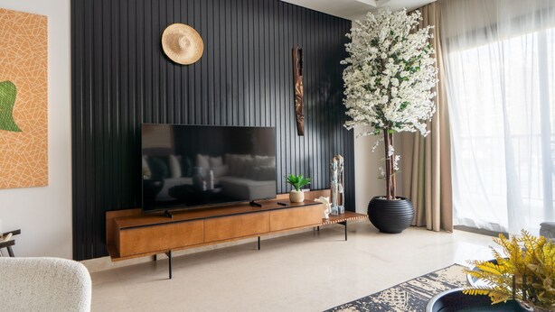 Een moderne woonkamer met een wand van donker houtfineer, een grote flatscreen-tv, een houten salontafel en een grote witte bloeiende plant.