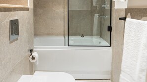 Een moderne badkamer met een douchecabine van glas, een wit toilet en een handdoekrek met witte handdoeken.