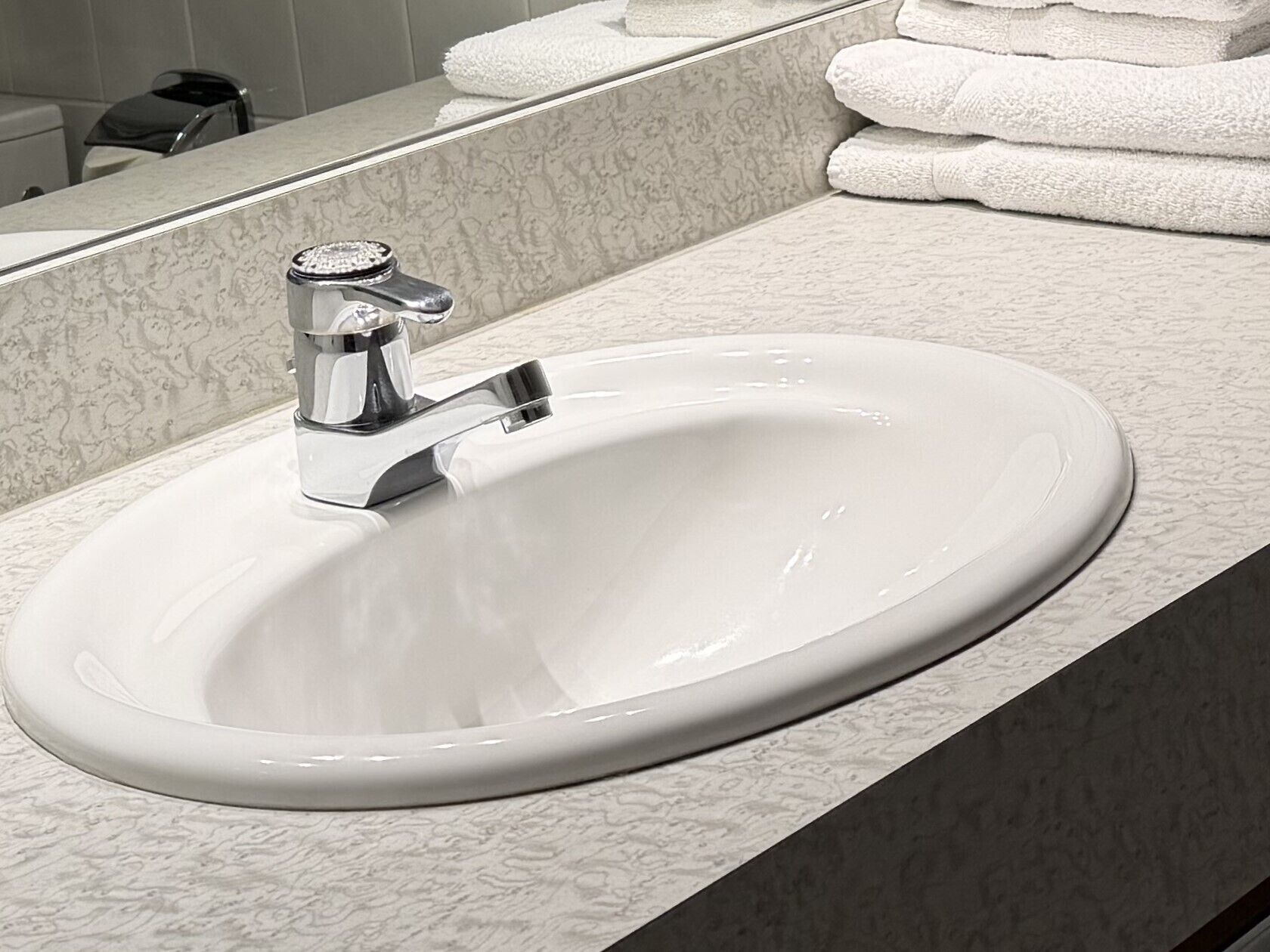 A bathroom sink with a chrome faucet, a mirror above it, and a stack of white towels.