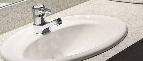 A bathroom sink with a chrome faucet, a mirror above it, and a stack of white towels.