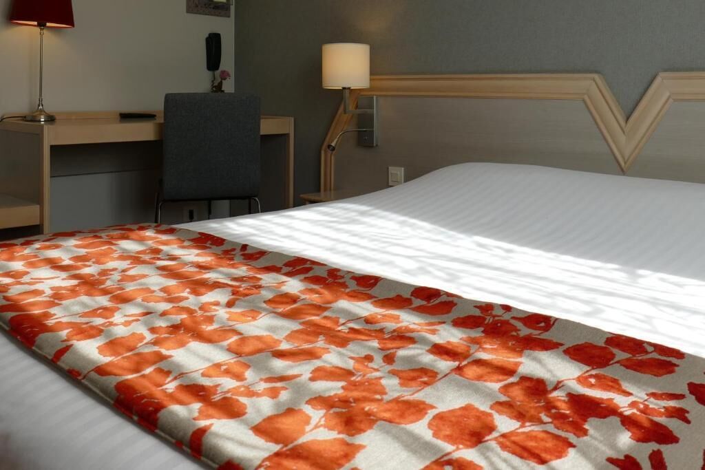 Una habitación de hotel con cama, escritorio, silla y lámpara.