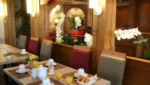 Une table dressée pour le petit-déjeuner, avec des assiettes, des tasses et un panier de viennoiseries.