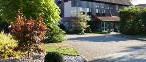 A hotel with a paved driveway, a large tree, and a well-maintained garden.