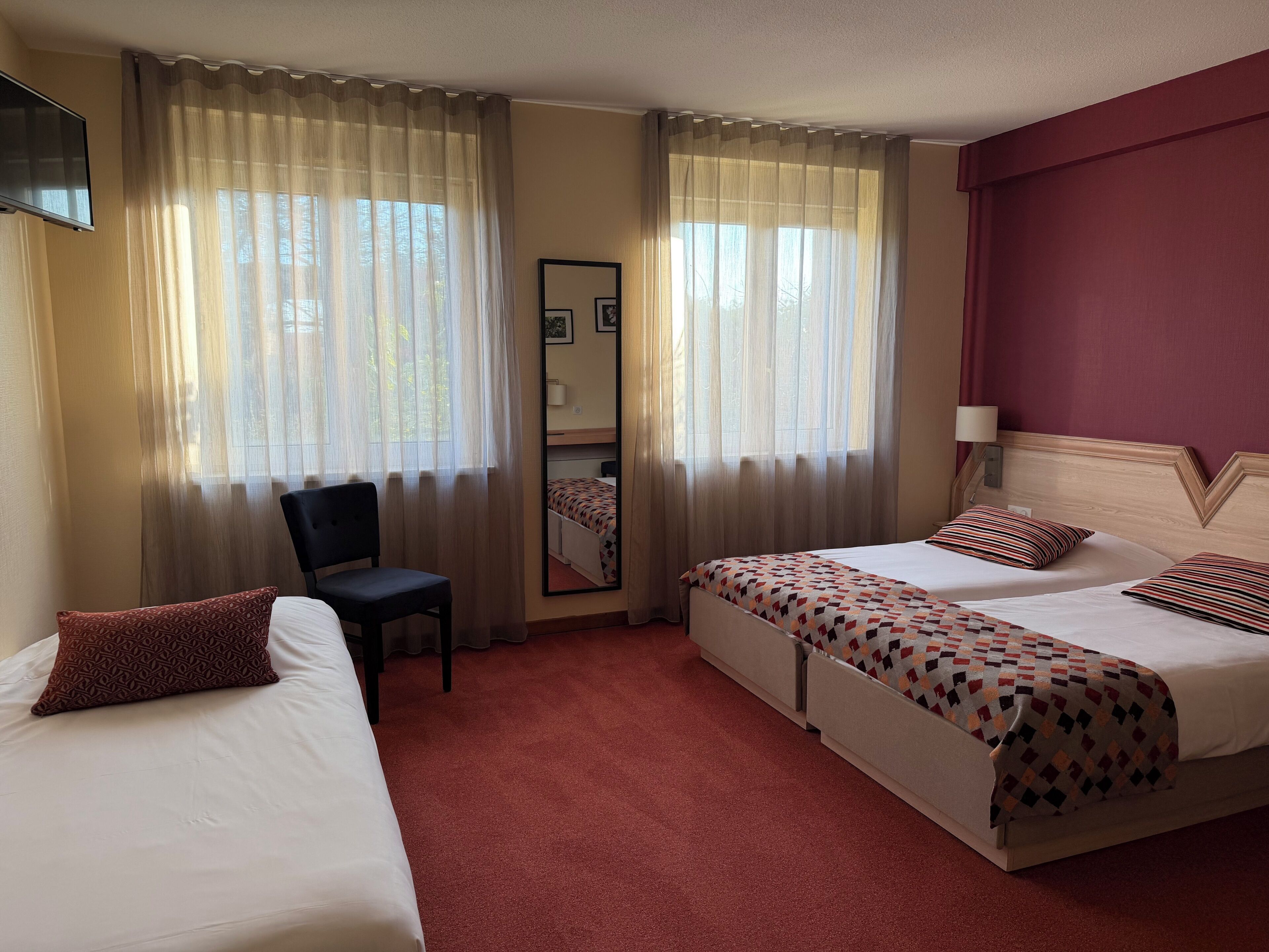 A hotel room with two beds, a chair, a mirror, and a television.