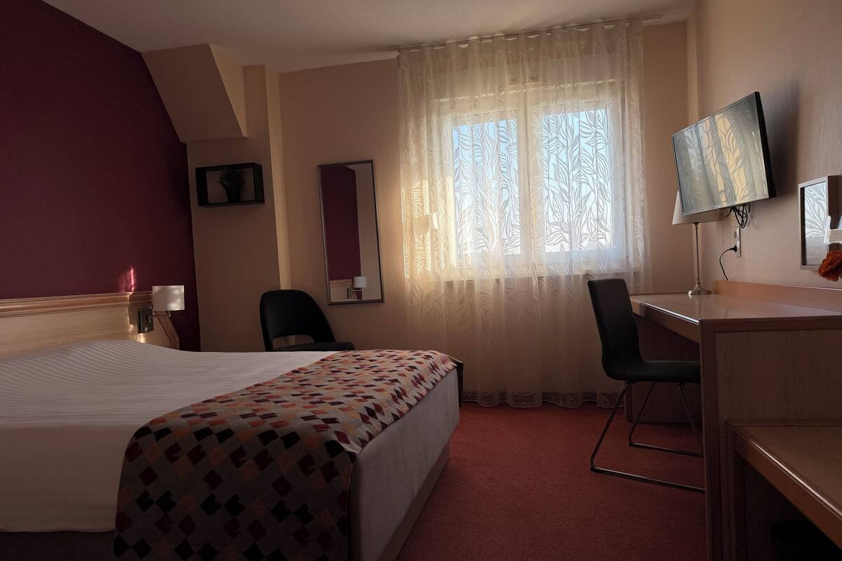 A hotel room with a bed, desk, chair, and a TV on the wall.