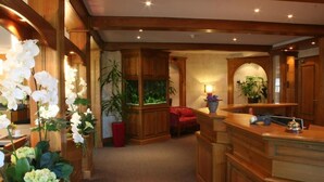 Un espace d’accueil avec un comptoir en bois, un fauteuil rouge, un aquarium et des plantes en pot.