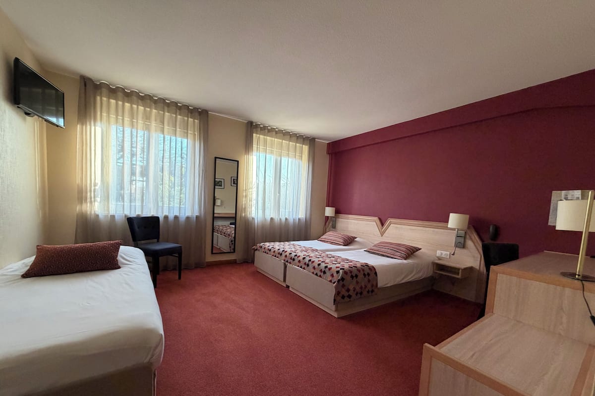 A hotel room with two beds, a desk, a chair, a TV, and a mirror.