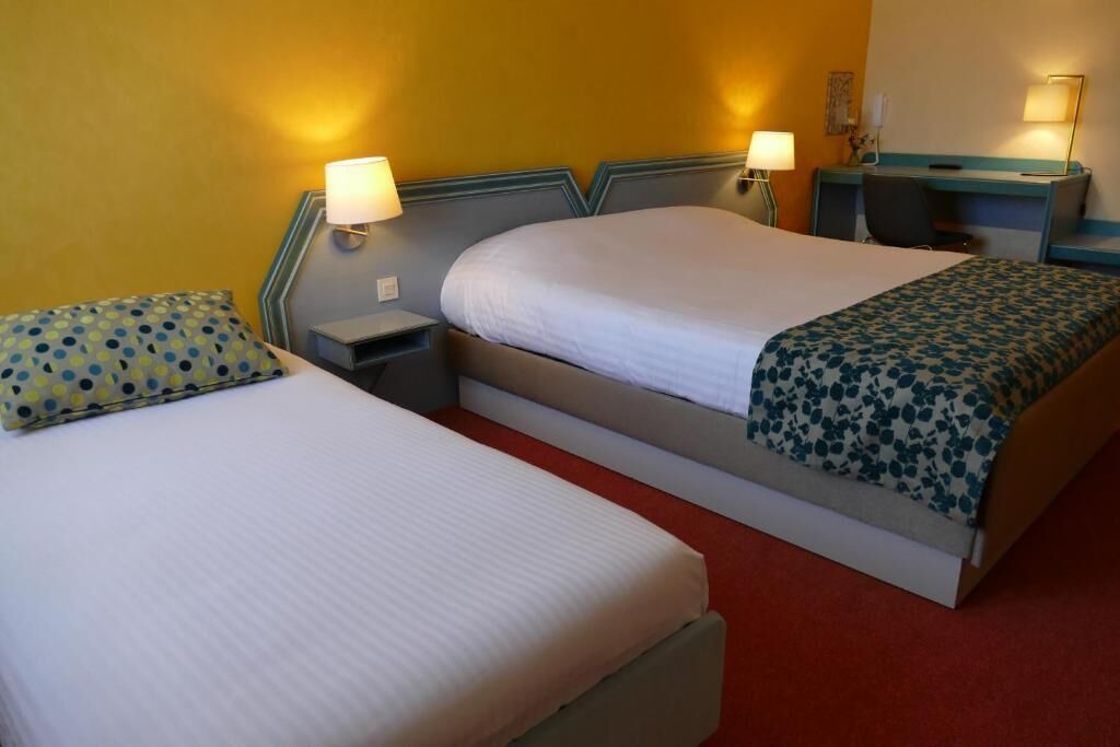 A hotel room with two beds, bedside tables, lamps, and a desk.
