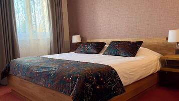Habitación de hotel con una cama grande, dos almohadas, una mesita de noche, una lámpara y un ventanal con cortinas.