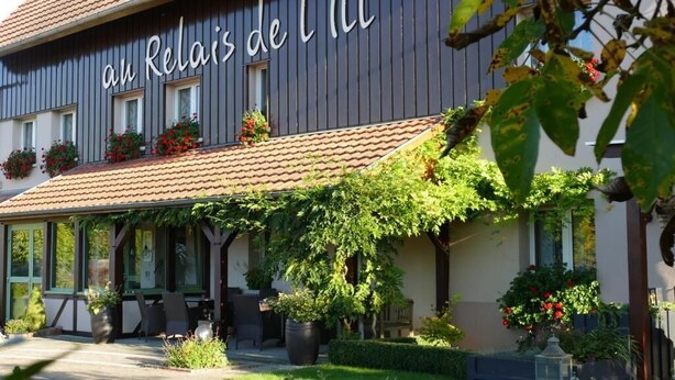 Un bâtiment portant une enseigne indiquant « Au Relais de l’Il », et doté d’un espace extérieur abrité avec des tables et des plantes en pot.