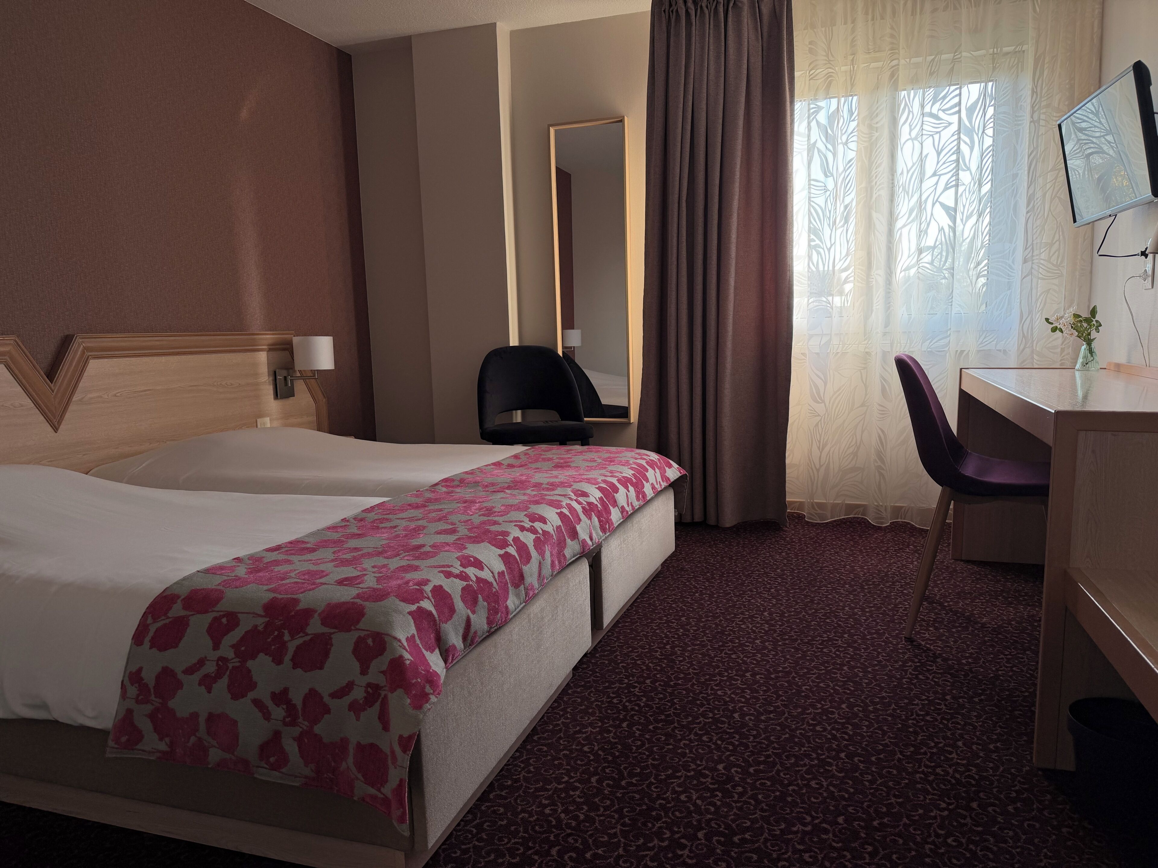 Ein Hotelzimmer mit zwei Betten, einem Schreibtisch, einem Stuhl, einem Fernseher und einem Spiegel.