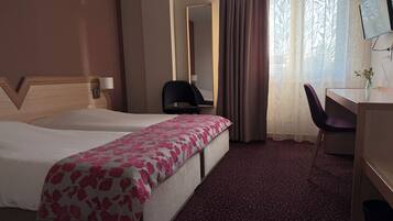 Ein Hotelzimmer mit zwei Betten, einem Schreibtisch, einem Stuhl, einem Fernseher und einem Spiegel.