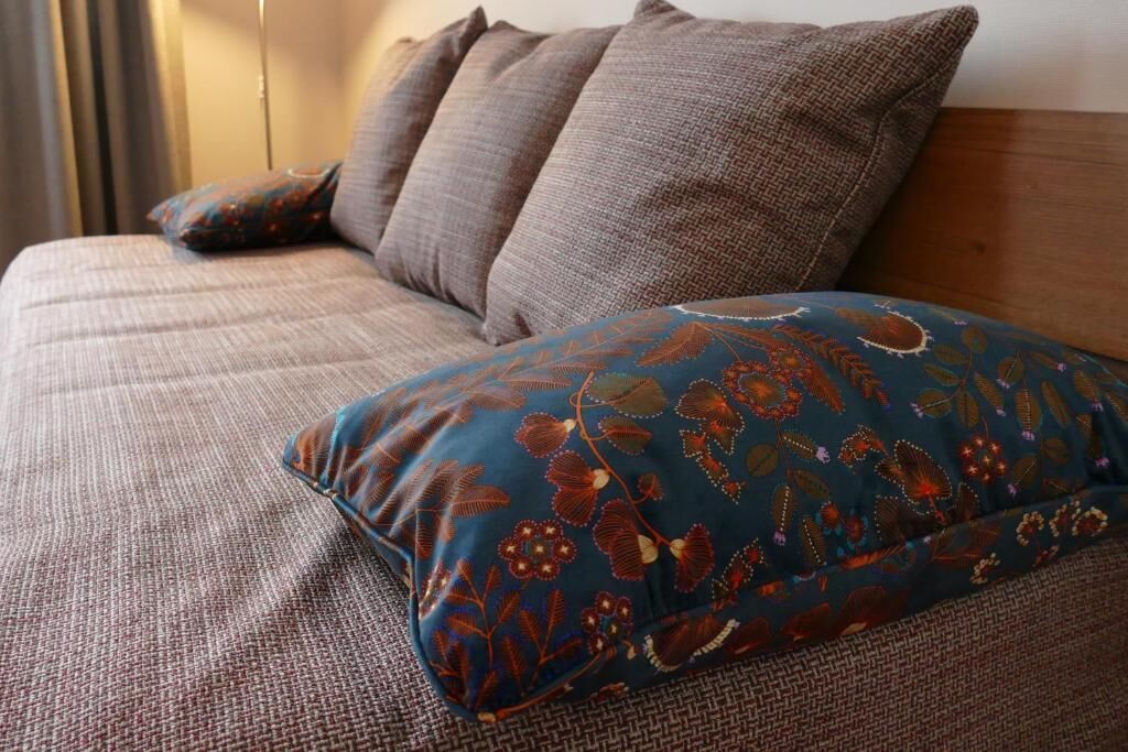 A bed with a patterned blue pillow and two brown pillows.