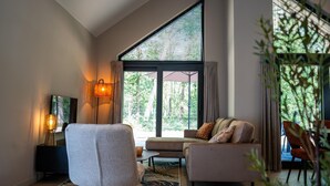 A modern living room with a large window, a sofa, a chair, a lamp, and a small table.