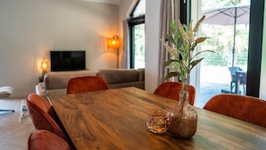 A dining area with a wooden table, red chairs, a vase with flowers, and a television in the background.