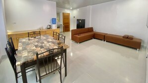 Un comedor con mesa y sillas, un sofá, dispensador de agua y refrigerador.