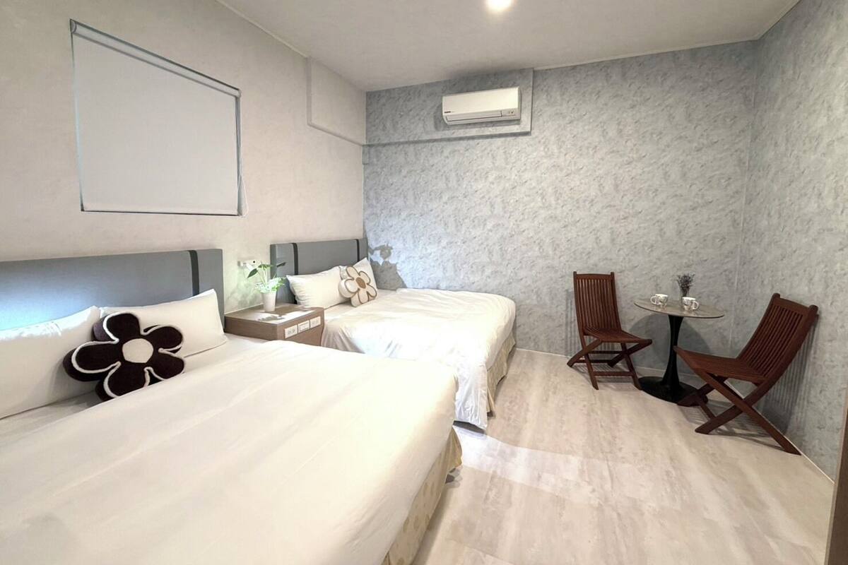Une chambre d’hôtel avec deux lits, une petite table avec des chaises, un appareil de climatisation et un cadre photo fixé au mur.